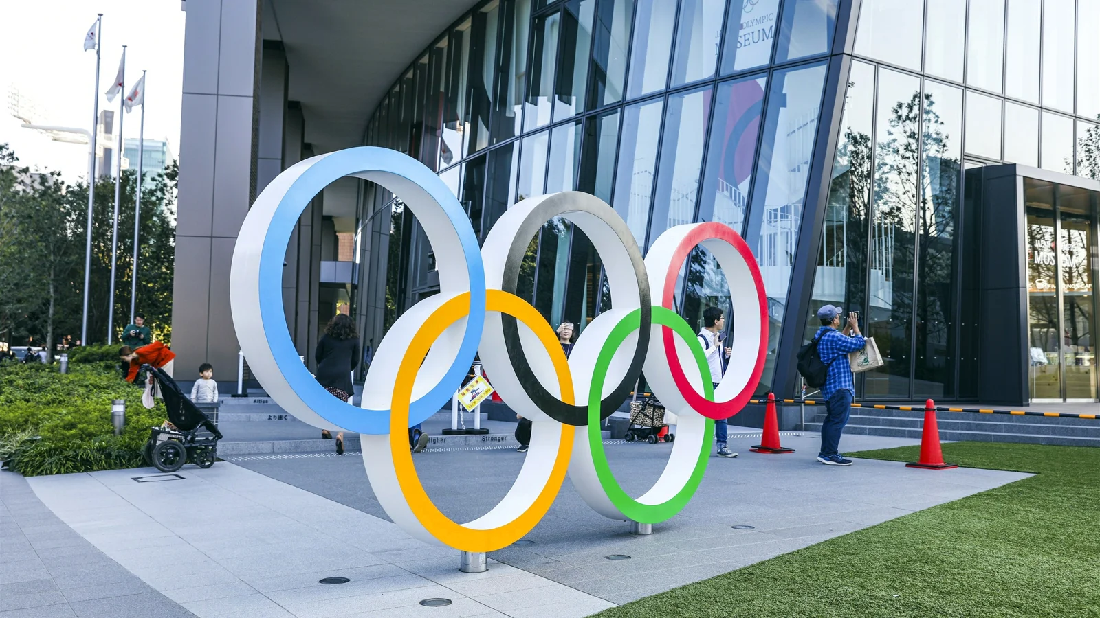 五彩奥运五环雕塑置于现代玻璃建筑前的户外广场上。