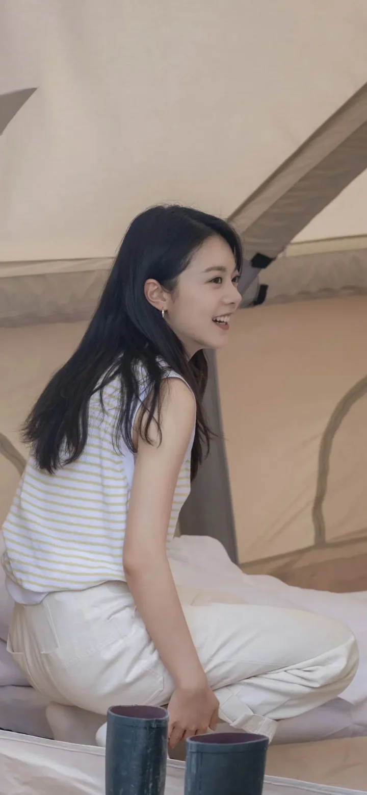一名女性坐在帐篷内，身穿浅色条纹上衣和白色长裤，面带微笑。