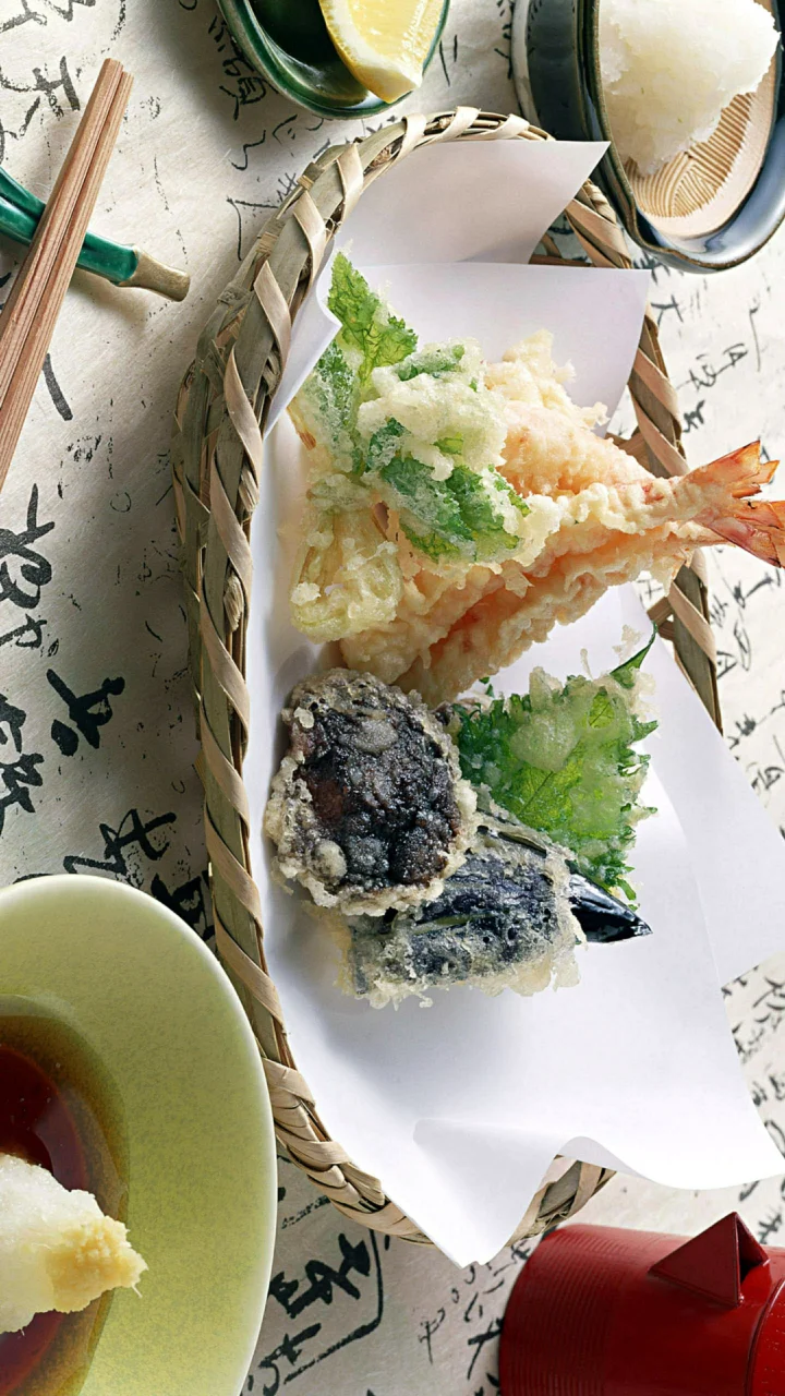 竹编篮中盛放着虾、鱼和蔬菜天妇罗，周围摆有餐具与蘸料碟。