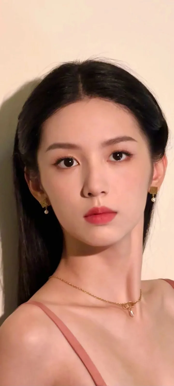 一名成年女性在浅色背景前的近距离肖像，佩戴耳环和细项链。