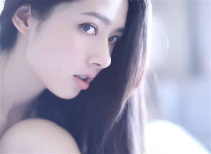 긴 머리의 여성이 부드러운 차가운 색감의 조명 아래 옆얼굴로 카메라를 바라보고 있습니다.