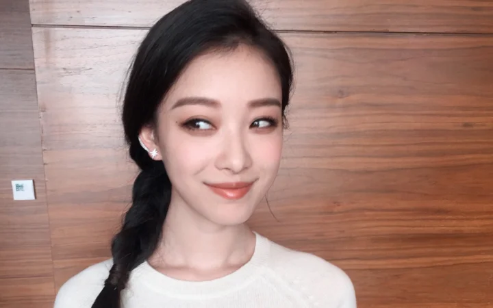一位成年女性在木质墙面前侧头微笑，黑发编成侧边辫子。