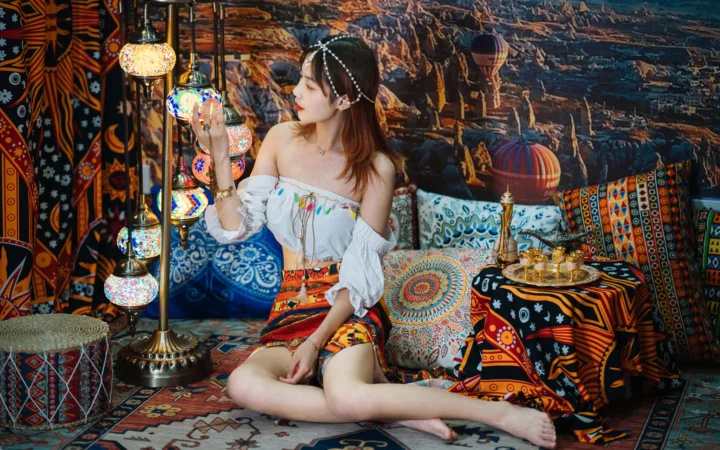 一名成年女性坐在铺满彩色图案的室内空间中，身旁悬挂着装饰灯具。