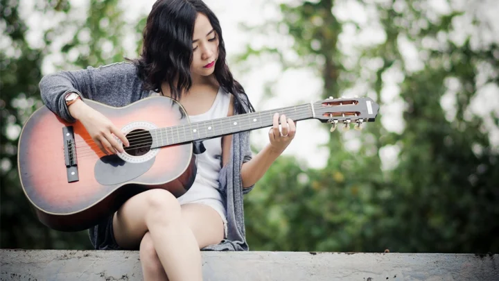 一名女子坐在戶外林間彈奏木吉他。