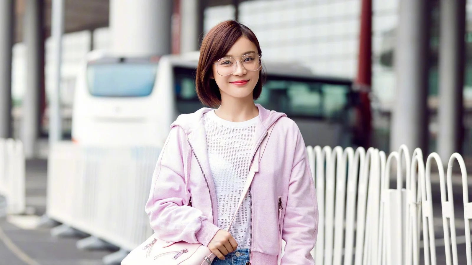 一名戴眼镜的成年女性站在户外建筑和车辆旁。