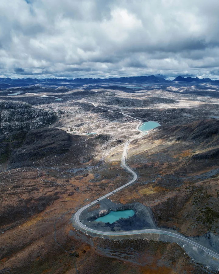 阴云笼罩的高原山地间分布着多个湖泊，一条蜿蜒公路穿过荒凉的棕色地表。