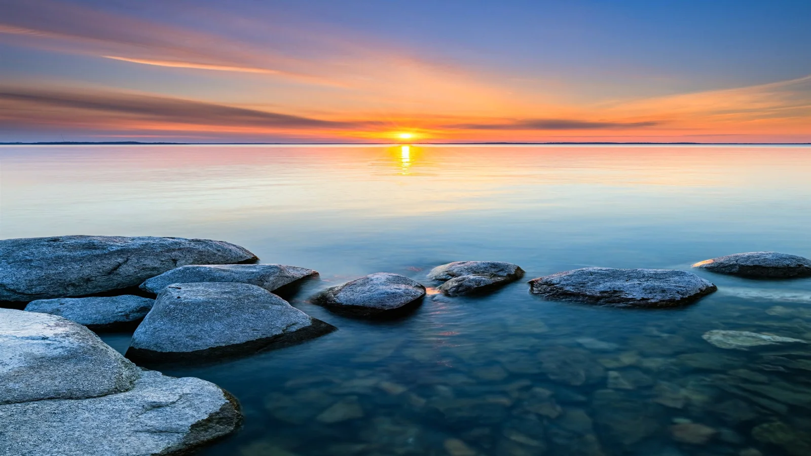 夕陽映照著平靜的水面，前景散布著深色礁石。