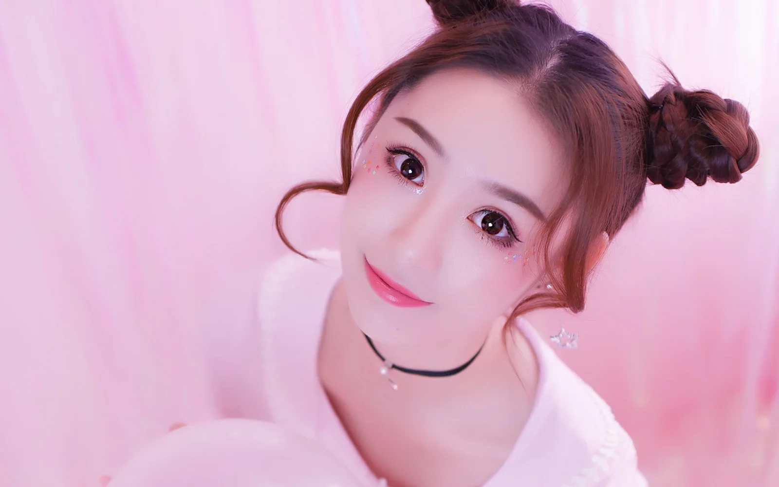 머리를 올린 여성이 전체적으로 분홍색인 배경 앞에서 카메라를 바라보는 클로즈업 인물 사진입니다.