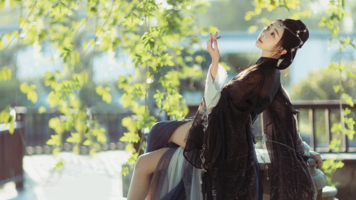 一名身穿深色传统服饰的女子坐在树影下，周围是明亮的绿色枝叶。
