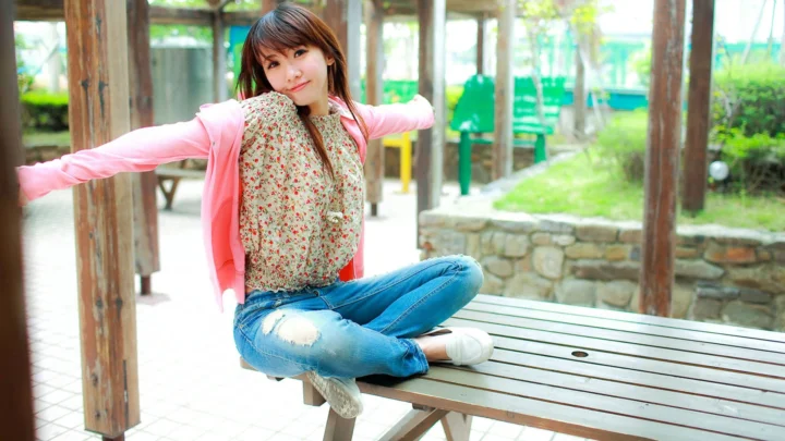 一名女子坐在户外木质长椅上张开双臂。