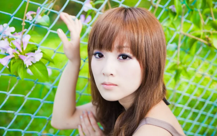 一名棕发女子在绿叶和紫色花朵映衬下望向镜头。