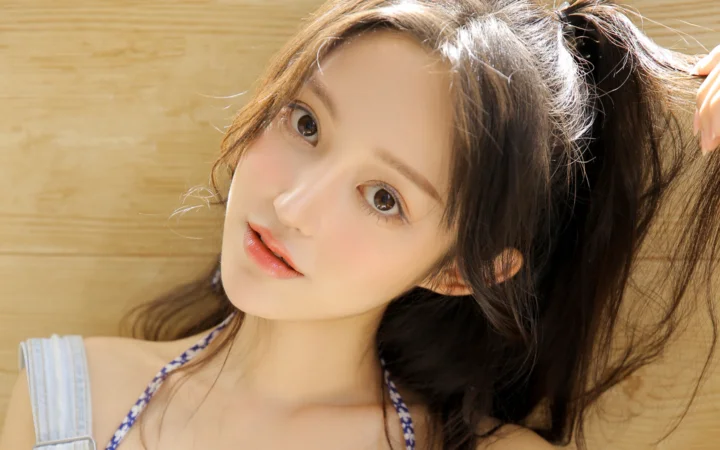 一名成年女性靠在木质背景前，抬头看向镜头并用手整理长发。