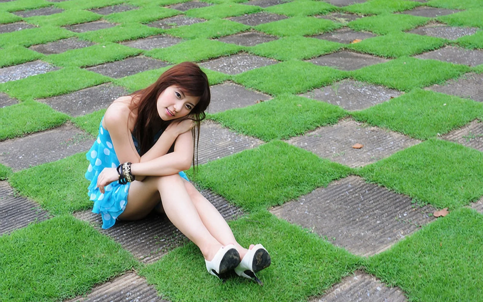一名身穿蓝色连衣裙的成年女子坐在铺有草坪的石板地面上。