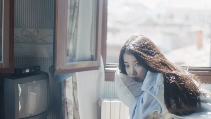 연한 색 목도리를 두른 성인 여성이 창가에 앉아 창밖의 햇빛이 실내로 들어오고 있습니다.
