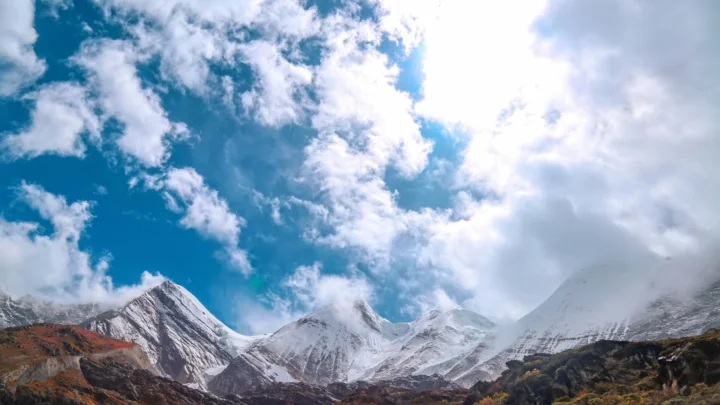 阳光穿透云层，照亮远处的雪山、秋色山谷与蓝天。