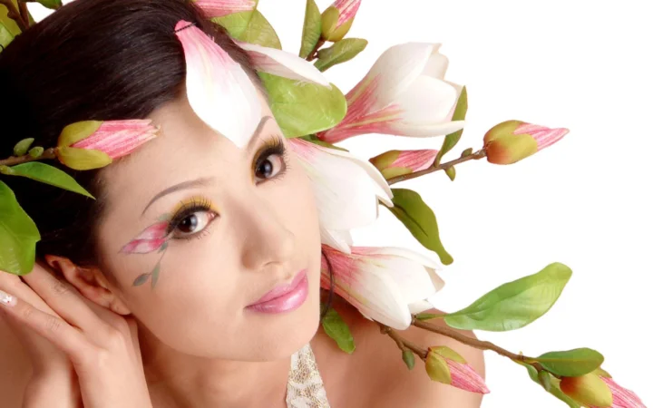 一名女性的面部特写被粉白色玉兰花和绿叶环绕。