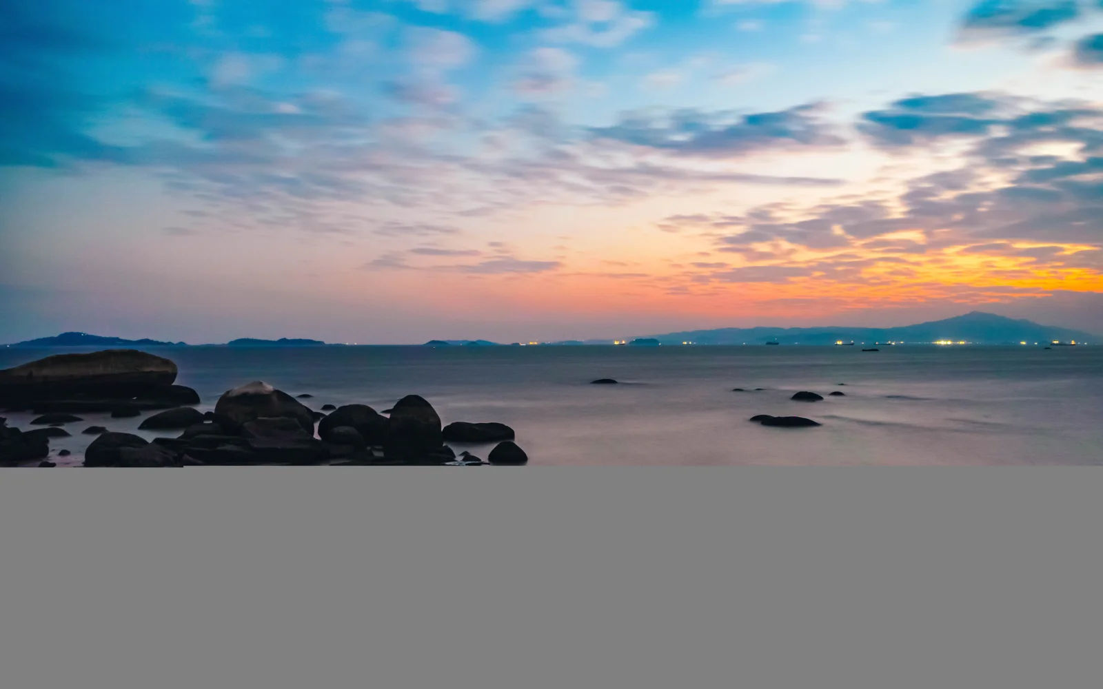 海と岩場、遠くの山並みが鮮やかな夕暮れの空に映えている。
