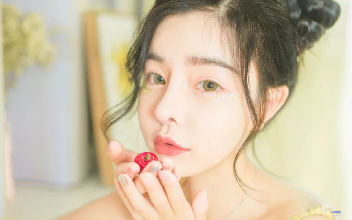 밝고 부드러운 배경 앞에서 빨간 과일을 든 성인 여성이 카메라를 바라보는 클로즈업 인물 사진입니다.