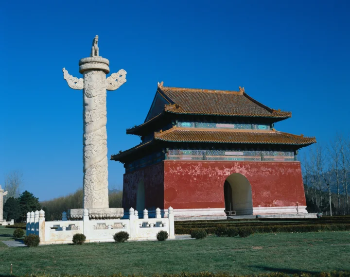 蓝天下，一座红墙古建筑与雕刻石柱坐落在修整整齐的草地旁。