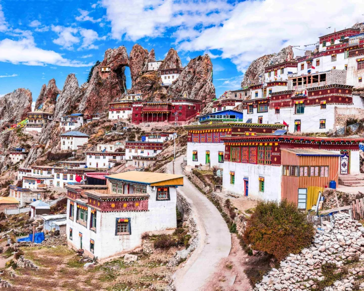 蓝天下，色彩鲜艳的藏式寺院建筑依山而建，周围环绕着陡峭的岩石山峰。