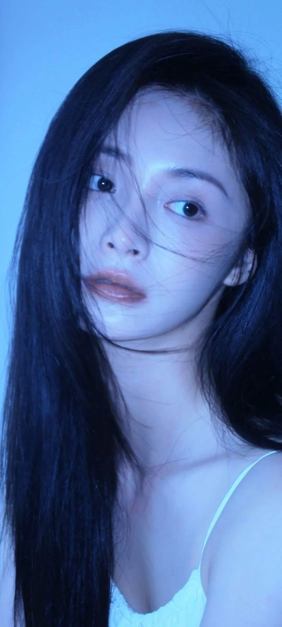 一位黑髮女性在藍色光線下進行近距離自拍式肖像拍攝。
