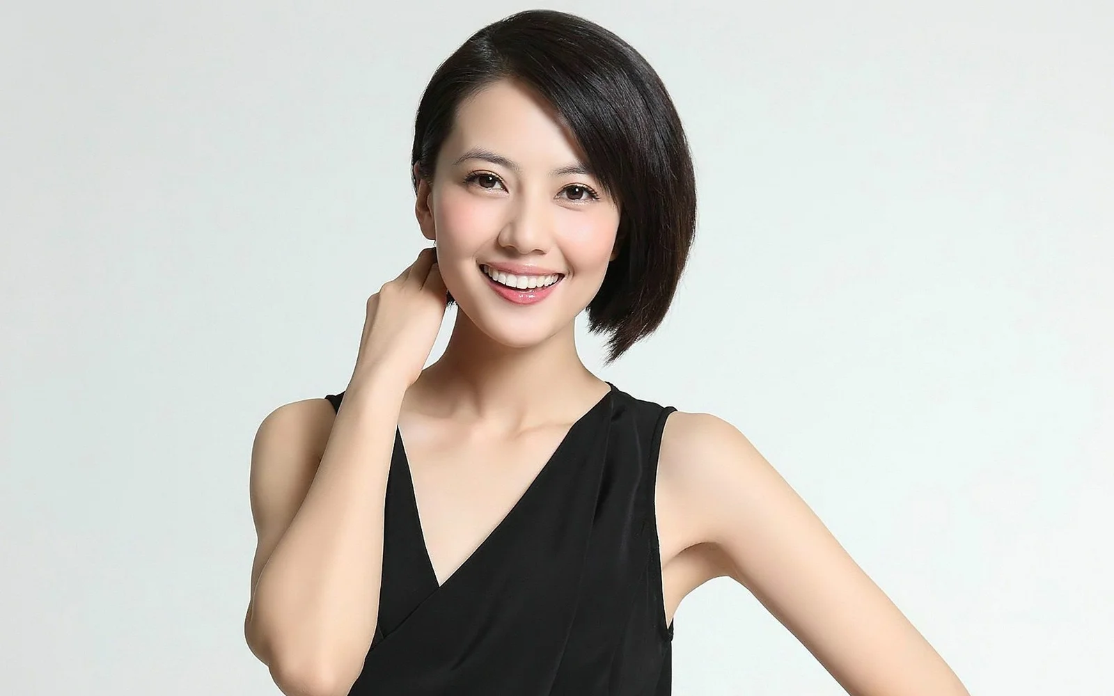 검은색 민소매 상의를 입은 성인 여성이 밝은 배경 앞에서 미소 짓고 있다.