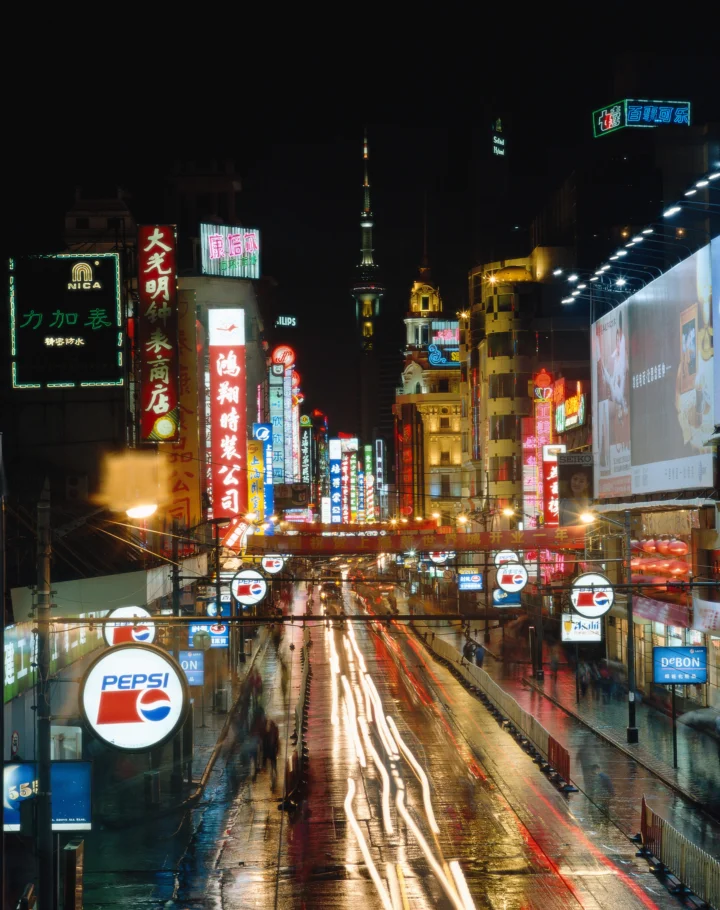 雨夜的城市街道两旁布满霓虹招牌，湿润路面倒映着绚丽灯光。
