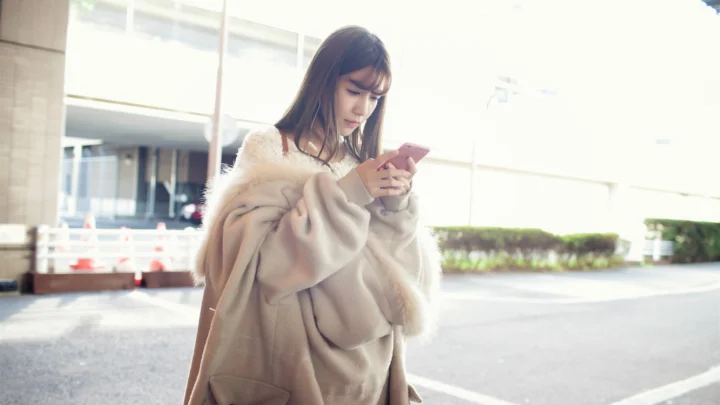 一名穿着浅色外套的女性在建筑外低头查看手机。
