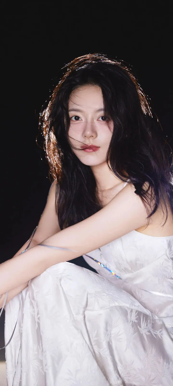 一名长发女性穿着白色礼服坐在黑色背景前。