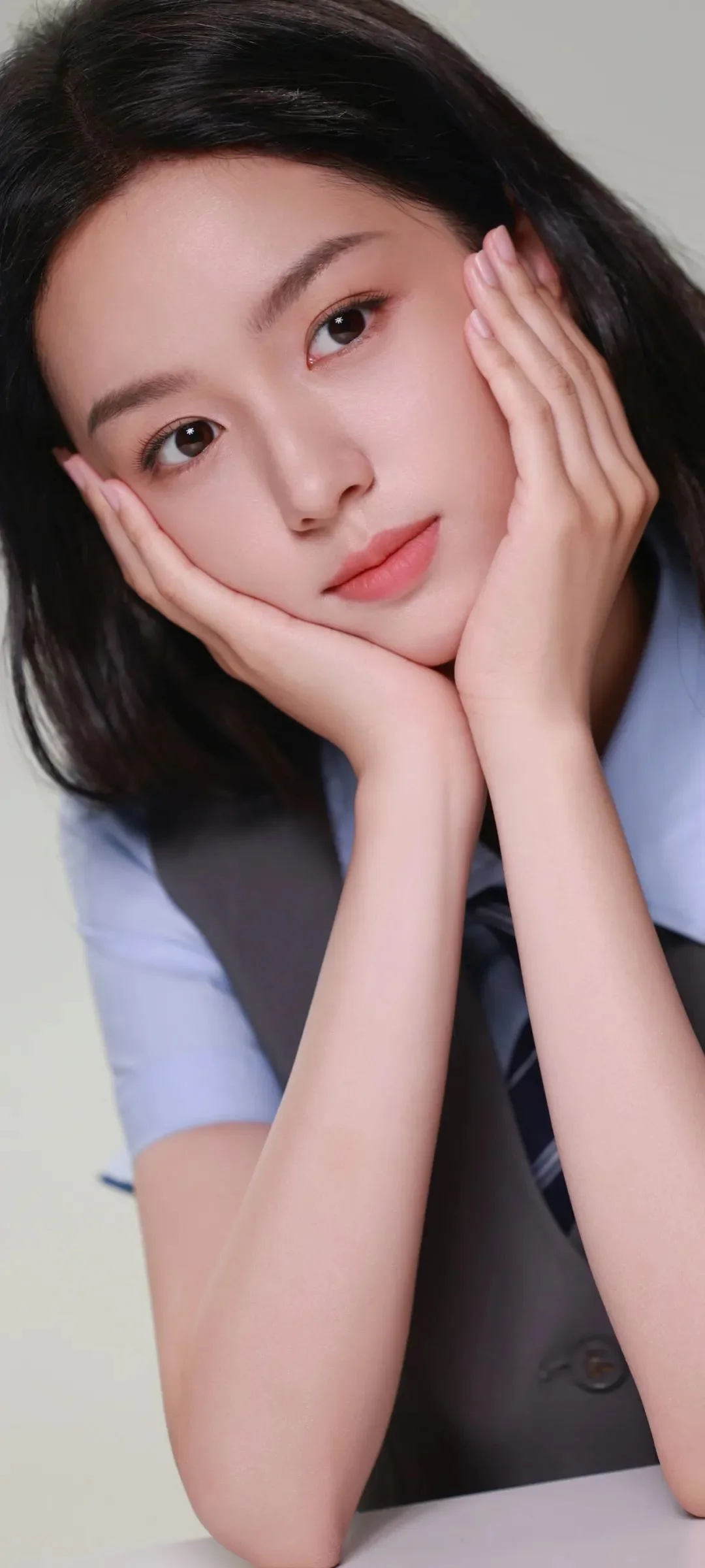 一名黑发女性用双手托着脸颊，面对镜头微笑。