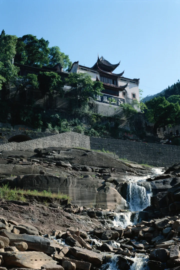 山间传统建筑坐落在树林与岩石溪流瀑布之上。