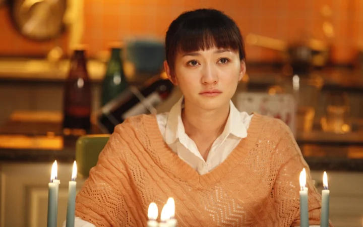 一名成年女性坐在温暖灯光和烛光映照的餐厅内。