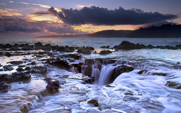 夕阳映照下的岩石海岸上，海水从礁石间形成层层瀑流。