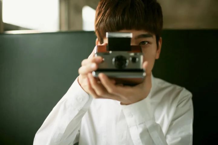 一名穿白衬衫的男子在室内举起一台即时成像相机对着镜头。