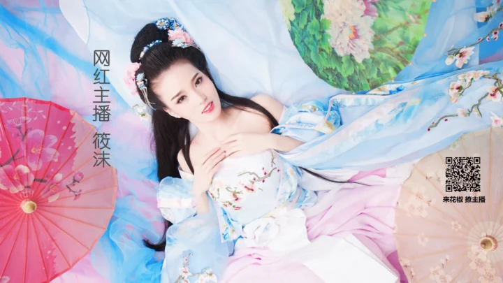 파란색과 흰색의 전통풍 의상을 입은 성인 여성이 꽃과 종이 우산 장식 사이에 누워 있습니다.