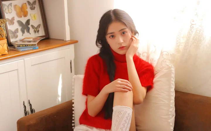 一名穿红色毛衣的女子坐在室内椅子上，阳光从窗边照入。