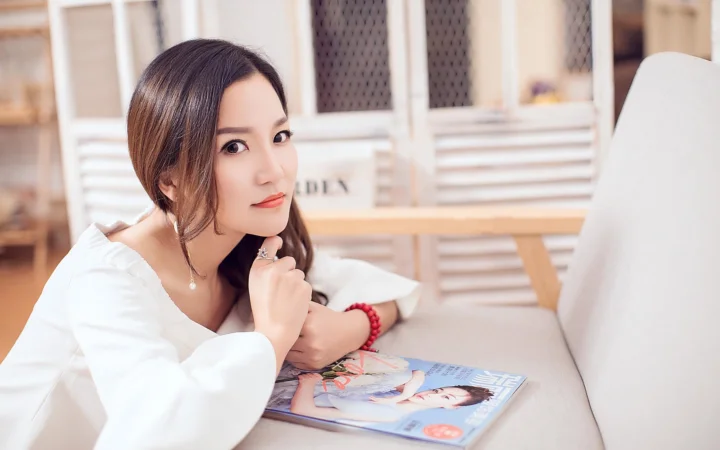 흰색 상의를 입은 성인 여성이 실내 소파에 기대어 카메라를 바라보고 있습니다.