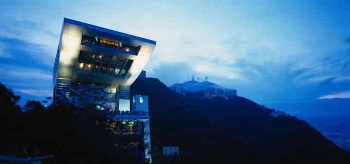 一座现代建筑坐落在山坡上，远处是朦胧山峦与蓝调天空。