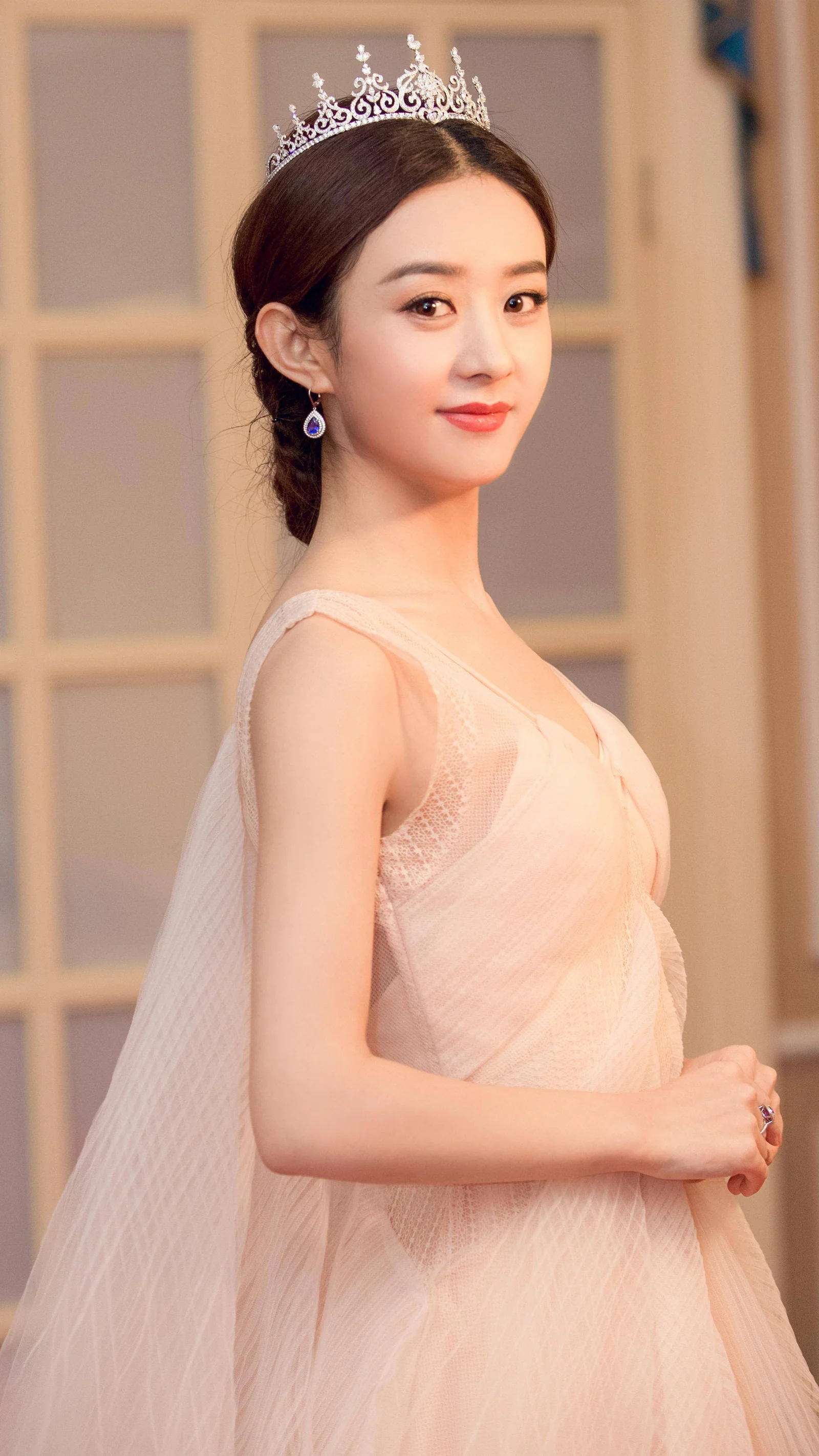 一位戴著皇冠、身穿淺色禮服的成年女性在室內回眸微笑。