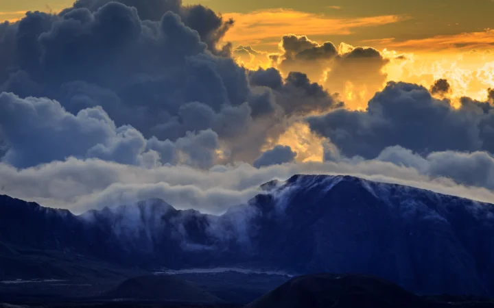金色夕阳穿透厚重云层，照亮远处深蓝色的山脉。