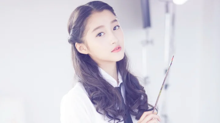 一名长发女子穿着白色上衣，手持画笔面向镜头。
