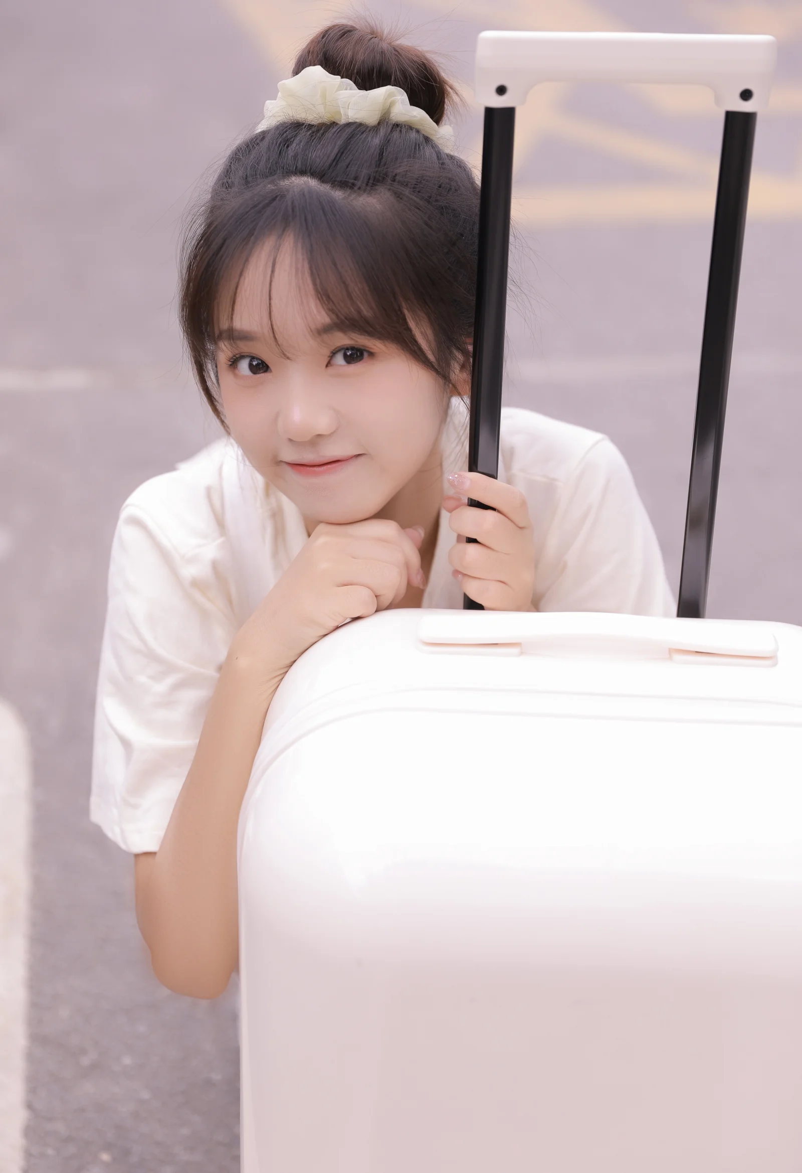 一名女性倚靠在白色行李箱旁并握着拉杆。