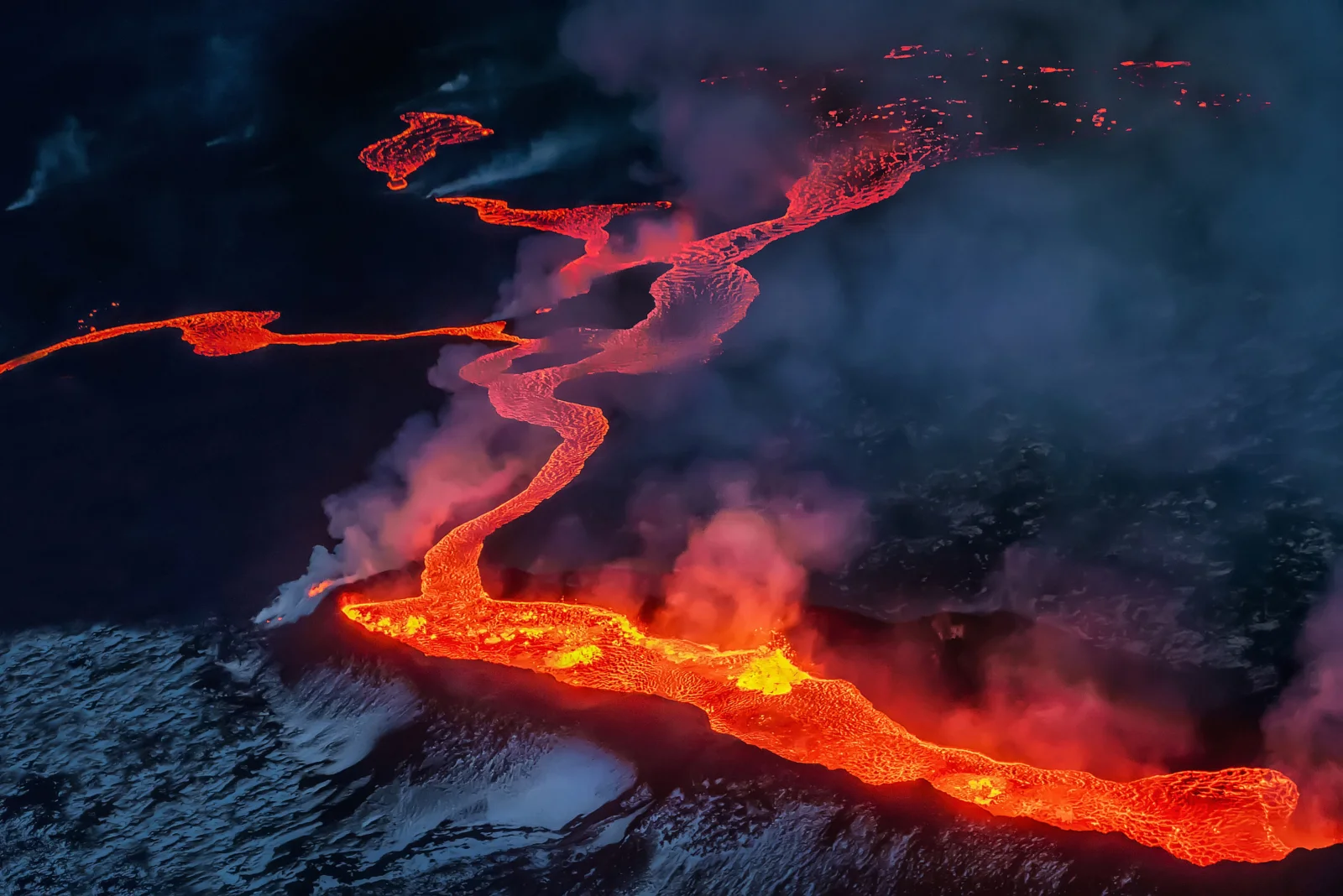 炽热的橙红色熔岩穿过黑暗的火山地表，周围升起浓烟。