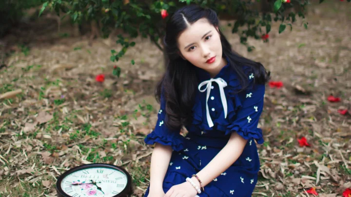 一名身穿蓝色连衣裙的女子坐在花园地面上，周围散落着红色花朵。