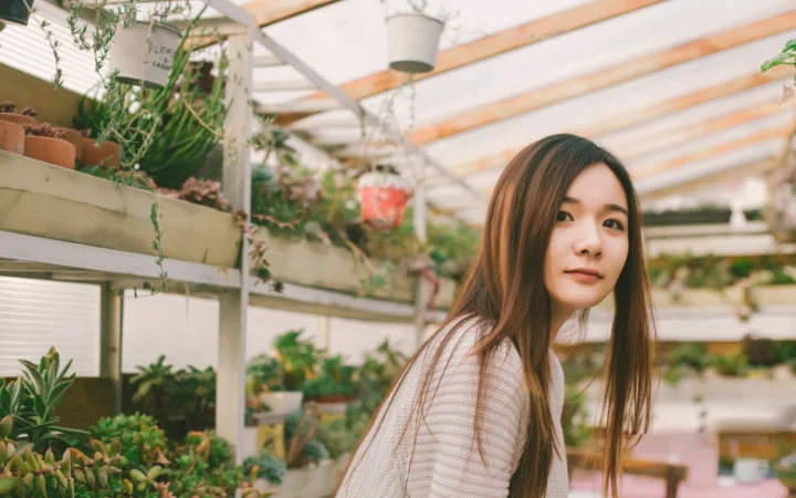 一名成年女性站在阳光充足的温室植物间。