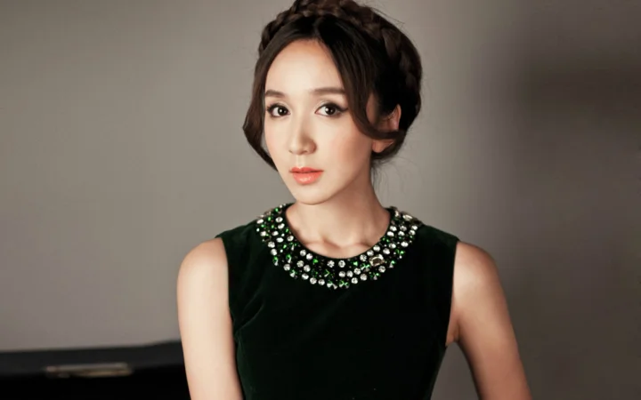 一名成年女性身穿饰有宝石领口的黑色无袖连衣裙，在室内背景前面向镜头。