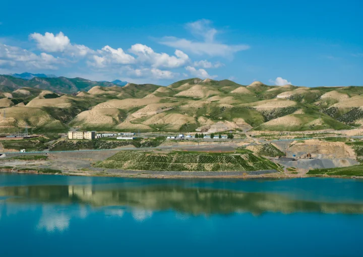 蓝色湖泊倒映着连绵起伏的山丘和云朵，远处可见田地与建筑。
