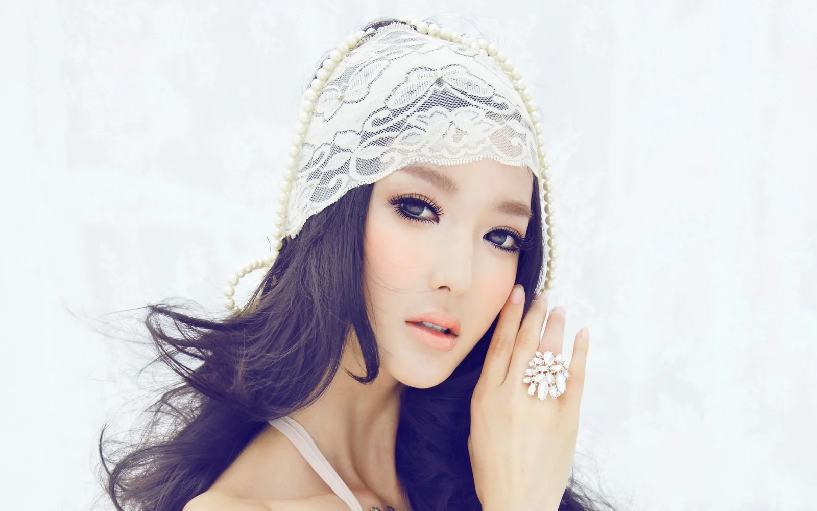 一名成年女性佩戴白色蕾丝头饰，以手轻触脸颊，呈现柔和明亮的人像特写。