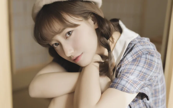 베레모와 체크무늬 셔츠를 착용한 여성이 팔에 기대어 카메라를 바라보고 있다.