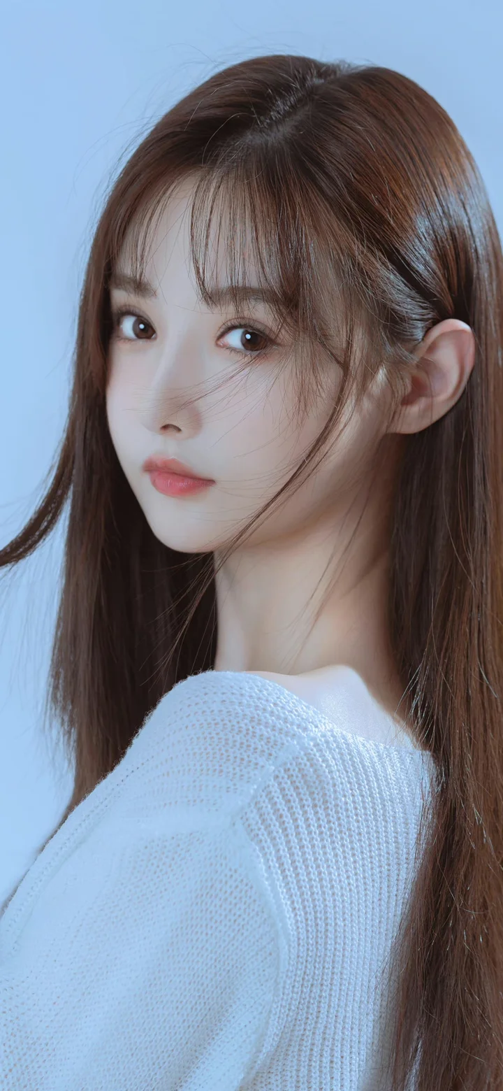 一名长发女性穿着白色针织衫，在浅蓝色背景前侧身看向镜头。